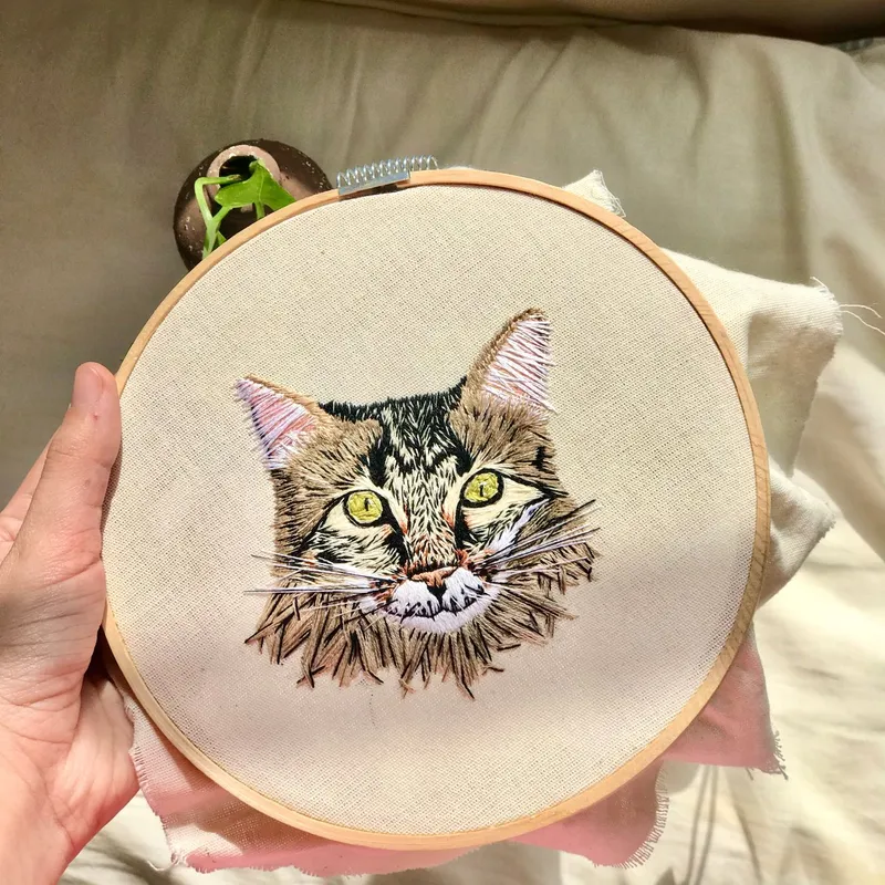 Close-up of a cat embroidered on fabric in a hoop, showcasing detailed craftsmanship.